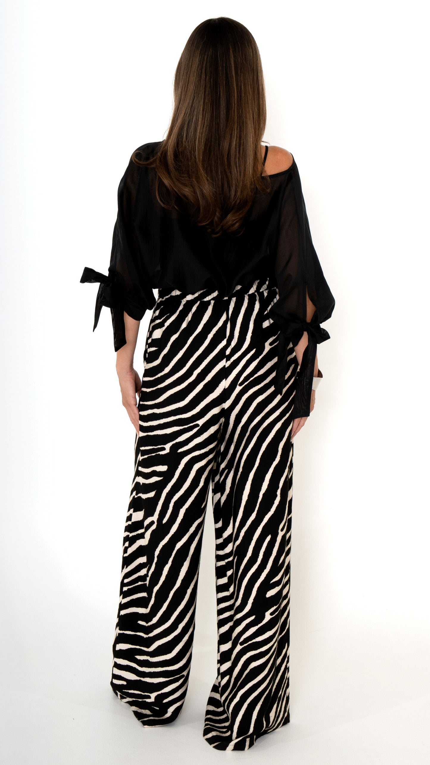 Rückansicht einer eleganten ausgefallenen Damenbekleidung in schwarz weiß: Modisch sommerliches Outfit bestehend aus einer weiten Zebra Print Hose und einer schwarzen Chiffonbluse mit Schleifen am Ärmel, Halbarm