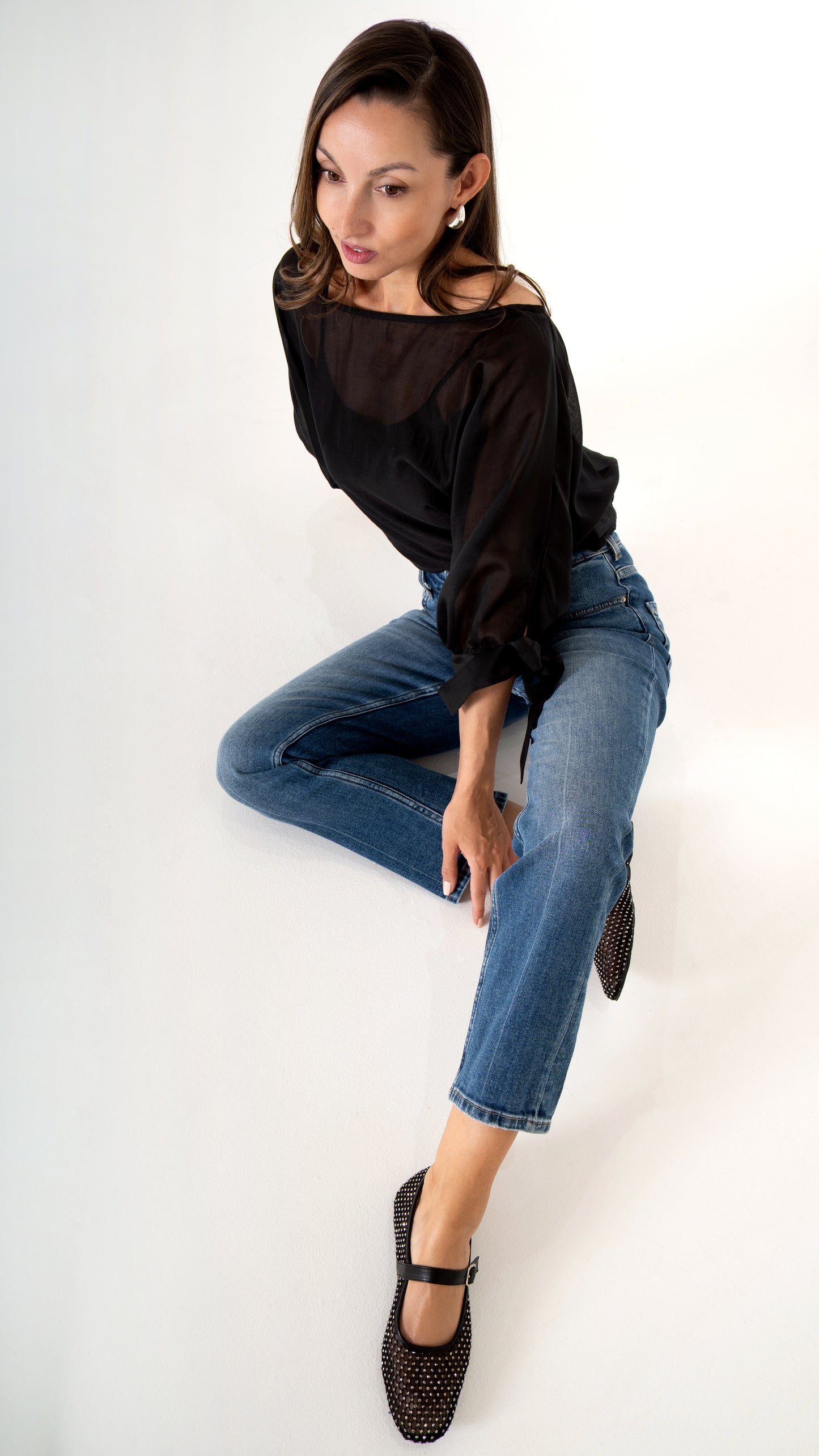 Feminine Damenkleidung sitzende Ansicht : gerade blaue Jeans verkürzt, schwarze Glitzer Mary-Jane- Ballerinas, Schwarze elegante Volumen Bluse leicht transparent