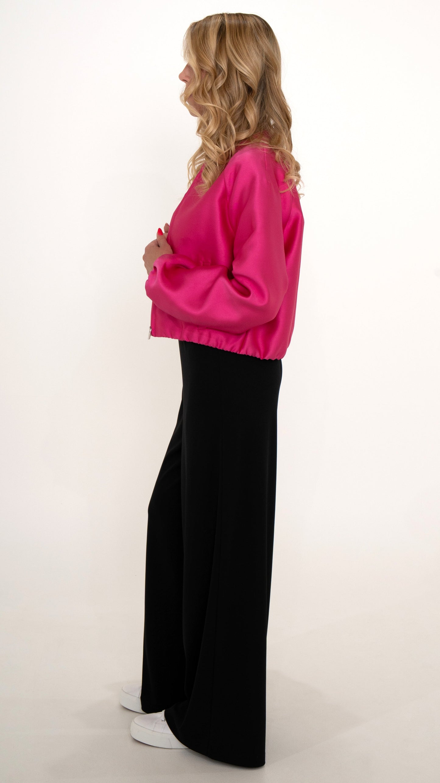 Elegante feminine Damenmode in leuchtendem Pink : Seitenansicht- Model trägt ein feminin schickes Outfit aus einer weiten schwarzen Hose mit einer leuchtenden Satin Glanz Blouson Bomberjacke
