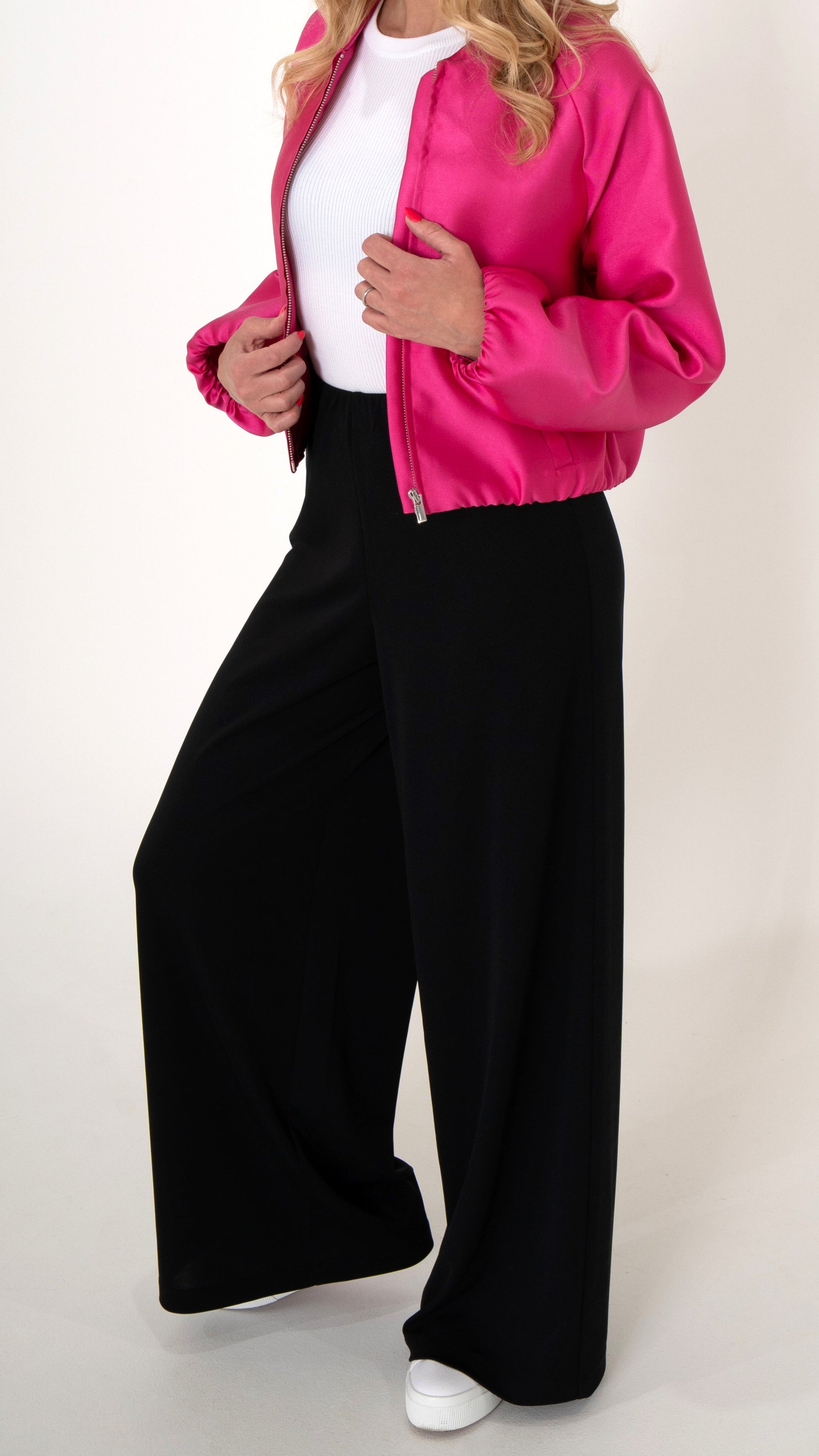 Damenkleidung : weite schwarze Hose mit einer pinken Bomberjacke mit leichtem Glanz. Darunter trägt das Model ein weißes Top